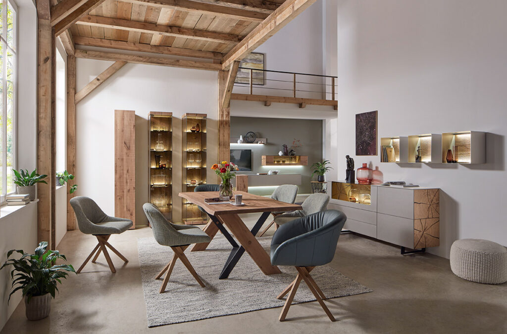 Modernes Esszimmer mit freiliegenden Holzbalken, einem Holztisch, grauen Stühlen, Pflanzen, Schränken und sanfter Beleuchtung. Neutrales Dekor.