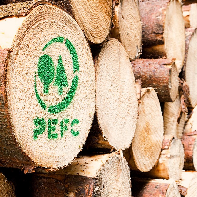 Gestapelte Baumstämme, auf deren Ende das PEFC-Logo aufgedruckt ist, mit zwei stilisierten Bäumen und Text.